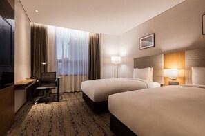 Une chambre d’hôtel avec deux lits, un bureau, une chaise, une télévision et une fenêtre avec des rideaux.