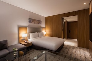 A modern hotel room with a large bed, bedside lamps, a small sofa, and a glass coffee table.