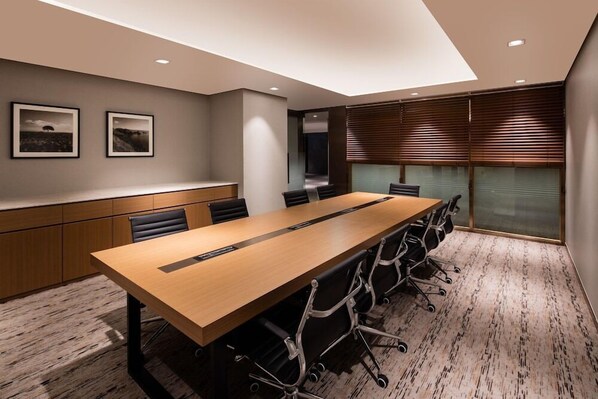 Un salón de conferencias con una larga mesa, sillas negras, armarios de madera y cuadros enmarcados en la pared.