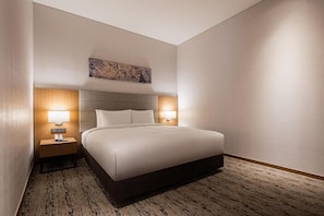A hotel room with a large bed, two bedside tables with lamps, a headboard, and a carpeted floor.