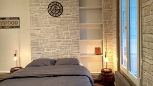 Ein Schlafzimmer mit Backsteinwand, einer Uhr, einem Regal und einem Fenster.