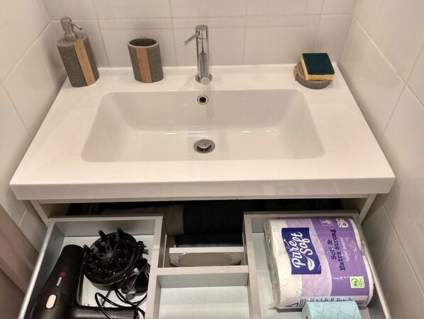 Ein Badezimmer mit einem weißen Waschbecken, einem Wasserhahn, einer Seifenspender und einem Toilettenpapierhalter.
