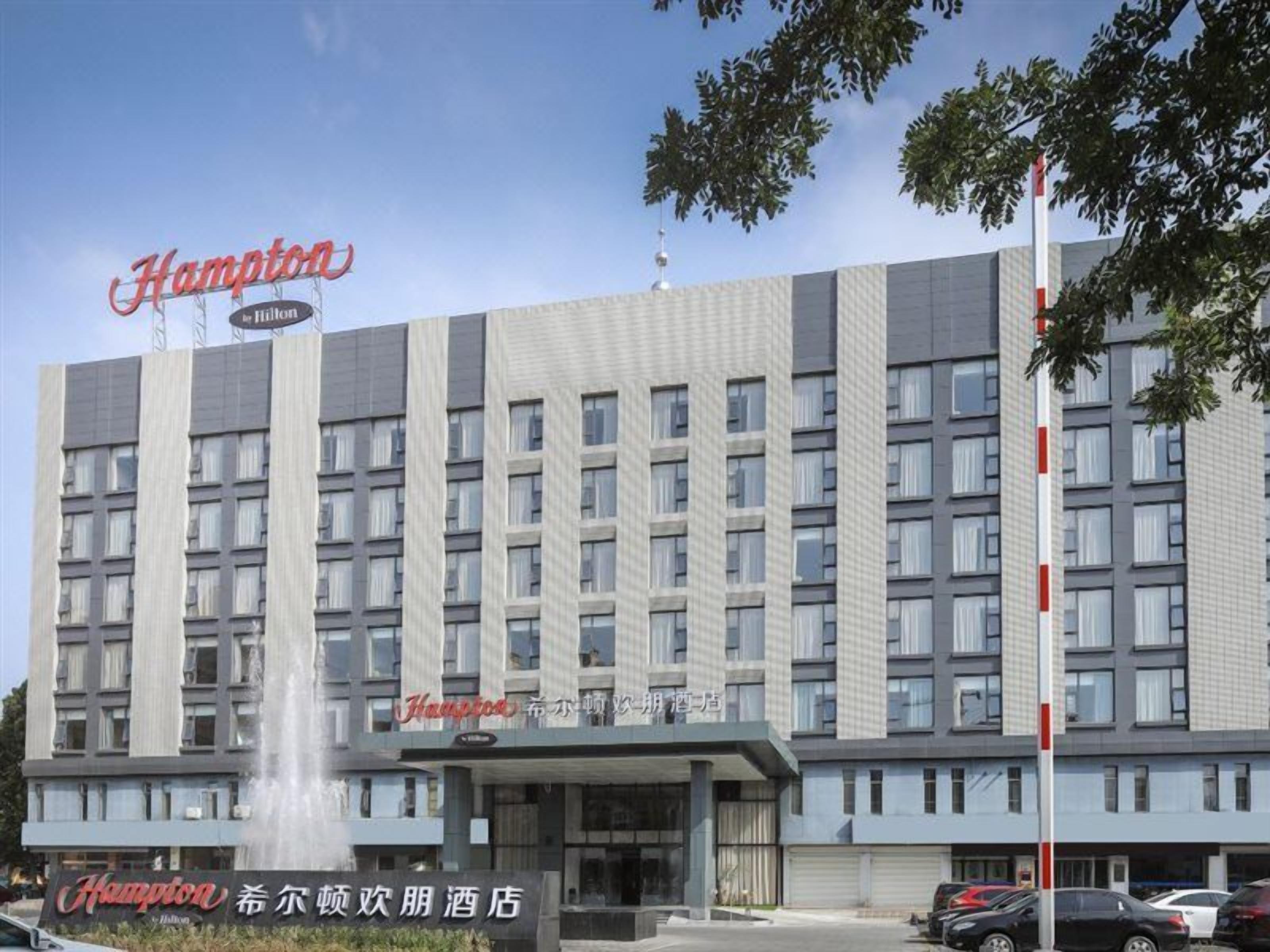A multi-story hotel with a prominent sign, a fountain, and a parking area.