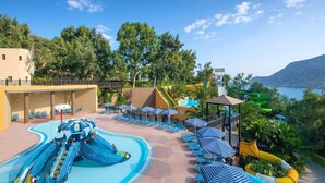 A resort pool area with a water slide, lounge chairs, umbrellas, and a view of the sea. - Fodele Beach Water Park Resort (Malevizi)