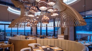 A modern restaurant with a curved seating area, wooden furniture, and a unique ceiling light fixture. - Fodele Beach Water Park Resort (Malevizi)