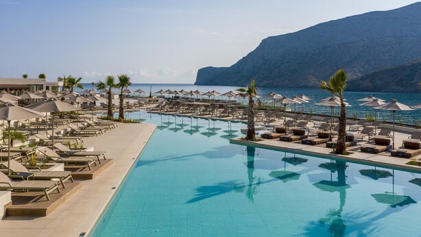 A resort pool area with sun loungers and umbrellas, overlooking a beach and mountains. - Fodele Beach Water Park Resort (Malevizi)