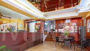 Vestíbulo de hotel con mostrador de recepción, una escalera y una zona de estar con sillas y una mesa.