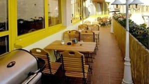 An outdoor dining area with yellow walls and striped awnings, featuring tables and chairs, and a grill. - Berliner Baer (Berlin)