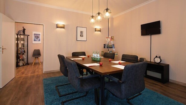 A dining area with a wooden table, six chairs, a blue rug, wall-mounted lights, and a flat-screen TV. - Berliner Baer (Berlin)