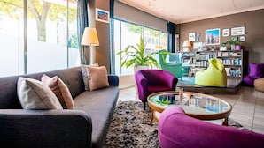 A modern living room with a grey sofa, a purple armchair, a yellow bean bag, and a glass coffee table. There is a bookshelf filled with books and a potted plant. - Berliner Baer (Berlin)