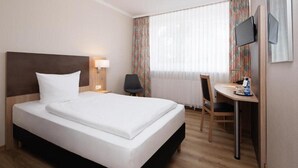 A hotel room with a bed, a desk, a chair, a TV, and a window with curtains. - Berliner Baer (Berlin)