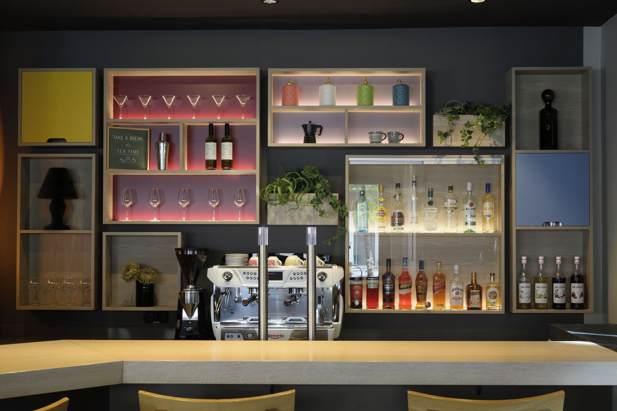 Una zona de bar con estantes llenos de botellas, vasos y una máquina de café.