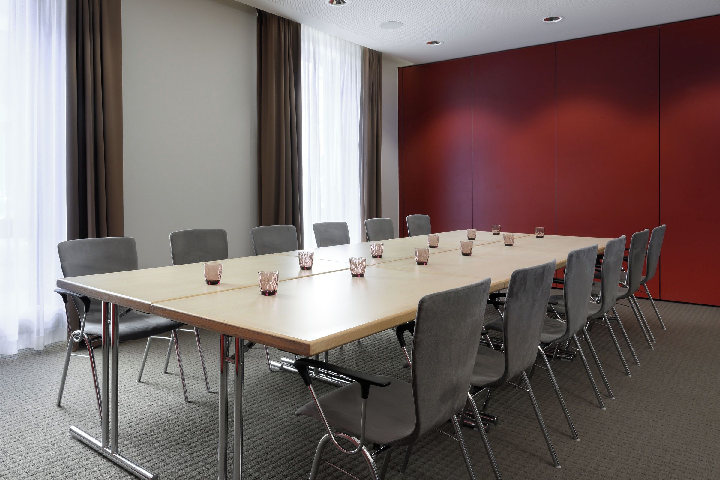 Uma sala de conferências com uma mesa comprida, cadeiras cinzentas e uma parede vermelha de destaque.