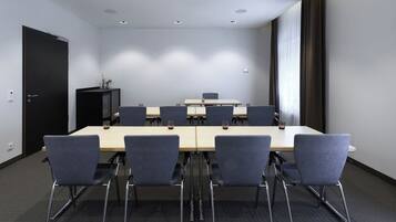 Un salón de conferencias con una mesa larga, seis sillas y un armario negro.
