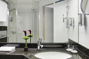 A modern bathroom with a granite countertop, a white sink, a glass shower enclosure, and a mirror with a chrome frame. - Leonardo Hotel Nürnberg City Center (Nuremberg)