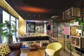 Una sala de estar moderna con un sofá, un sillón y una mesa de centro. Se ve una estantería con varios objetos y un televisor.