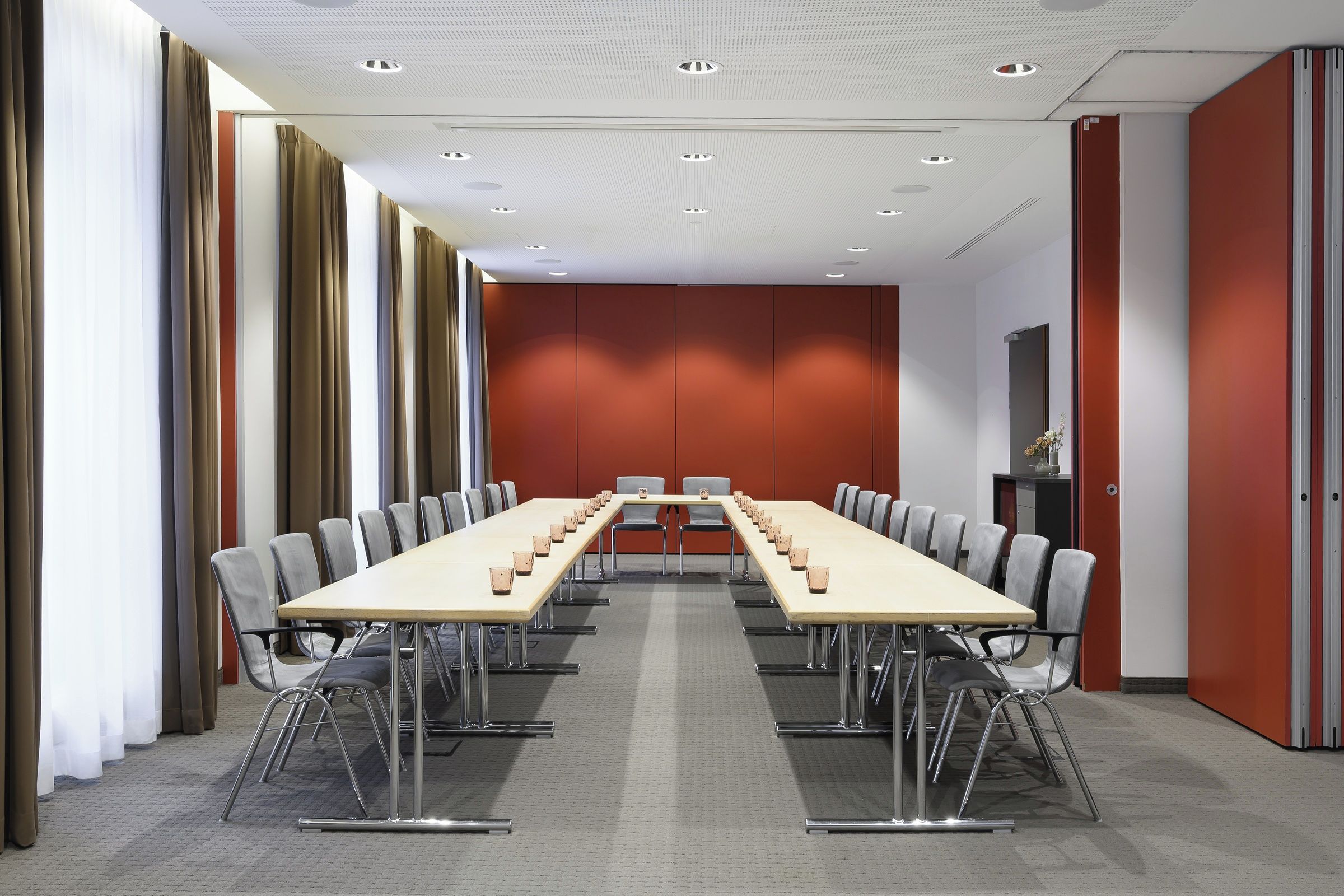 Una sala de conferencias con una larga mesa y sillas, una pared de acento roja e iluminación empotrada en el techo.