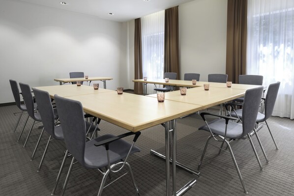A conference room with a long table, grey chairs, and a carpeted floor.