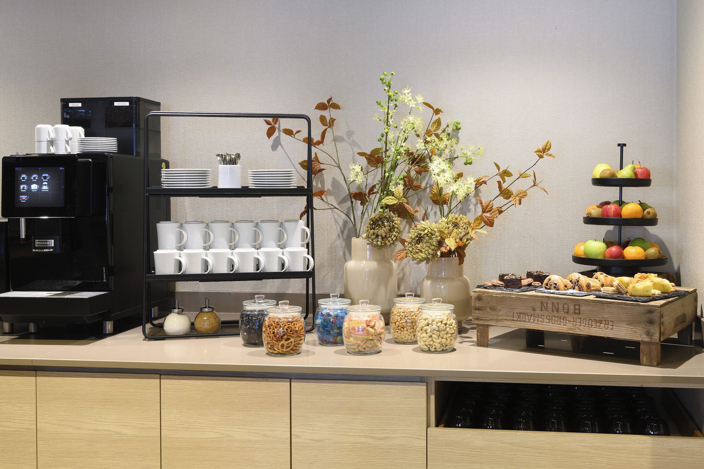 Estação de pequeno-almoço com serviço próprio, com máquinas de café, chávenas e uma exposição de fruta.