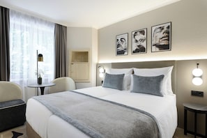 A hotel room with a bed, bedside tables, a chair, a desk, and artwork on the wall. - Leonardo Hotel Nürnberg City Center (Nuremberg)