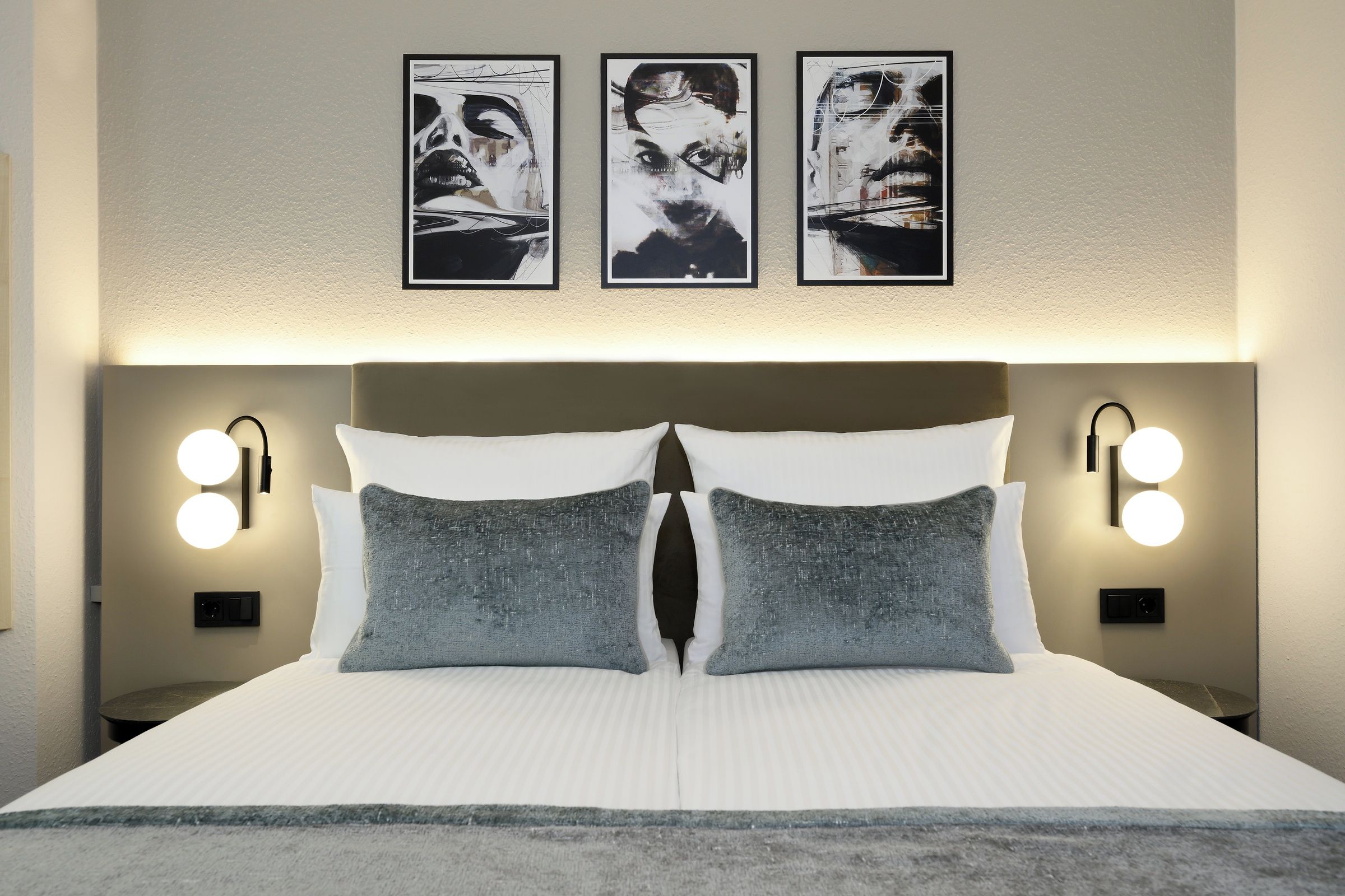 Habitación de hotel con una cama grande, dos almohadas, cabecera con iluminación integrada y tres obras de arte enmarcadas en la pared.