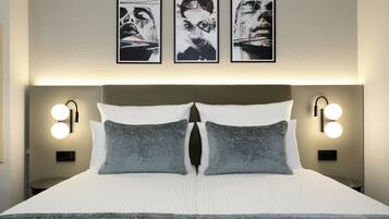 Habitación de hotel con una cama grande, dos almohadas, cabecera con iluminación integrada y tres obras de arte enmarcadas en la pared.