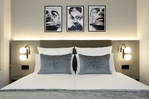 Camera d'albergo con un letto grande, due cuscini, una testiera con illuminazione integrata e tre opere d'arte appese alla parete.