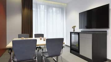 Una sala de conferencias con una mesa, sillas, una televisión y un minibar.