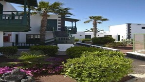 A courtyard with a staircase leading to a balcony, surrounded by palm trees and flowering plants. - Los Pueblos Apartments (Tías)