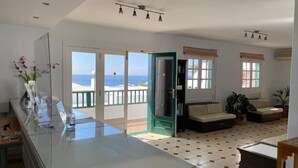A spacious living area with a glass partition, a sofa, a coffee table, and a view of the sea. - Los Pueblos Apartments (Tías)