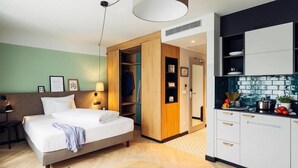 A hotel room with a bed, a desk with a laptop, a closet, and a kitchenette. - Harry's Home Berlin - Moabit Hotel & Apartments (Berlin)