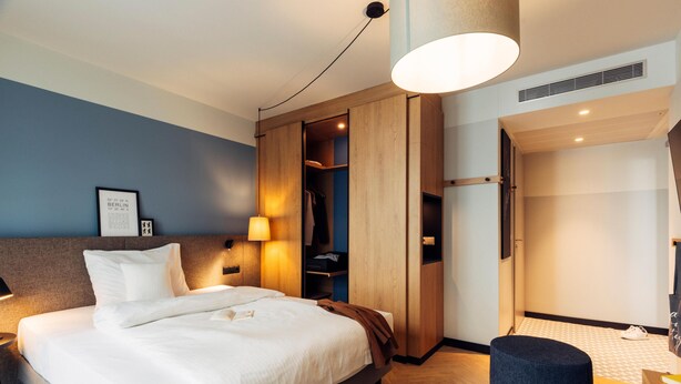 A modern hotel room with a bed, bedside table, lamp, wardrobe, and a small seating area. - Harry's Home Berlin - Moabit Hotel & Apartments (Berlin)