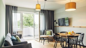 A modern living room with a sofa, a dining table with chairs, a television, and a sliding glass door leading to an outdoor area. - Harry's Home Berlin - Moabit Hotel & Apartments (Berlin)