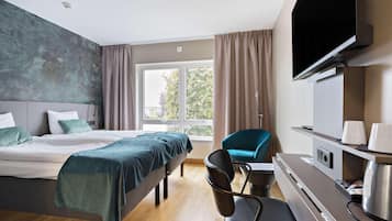 Ett modernt hotellrum med en säng, ett skrivbord med en kaffemaskin, en TV och utsikt över omgivningarna.