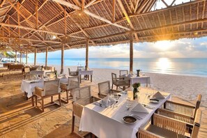 An outdoor dining area with tables set for two, overlooking a beach.