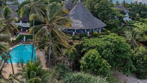 Ein Resort mit Swimmingpool, umgeben von Palmen und Gebäuden mit Strohdächern.