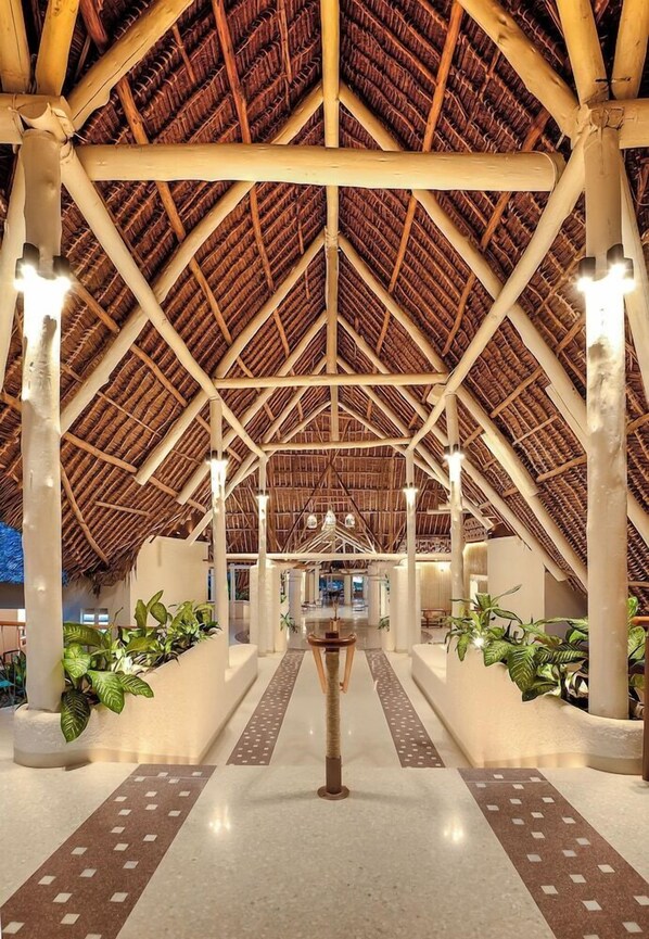 A covered atrium with a high ceiling, structural beams, and potted plants.