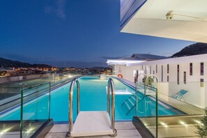Una piscina en la azotea con barandillas de vidrio, una vista despejada del paisaje urbano y un diseño arquitectónico moderno.