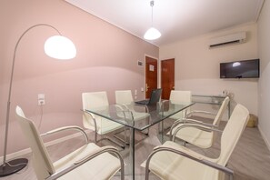 Une salle de conférence équipée d’une table en verre, de chaises blanches, d’un ordinateur portable, d’un téléviseur à écran plat et d’un appareil de climatisation.