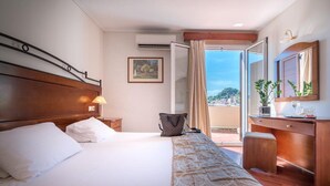 A hotel room with a bed, a desk, a chair, a window with curtains, a plant, and a painting on the wall. - Diana Hotel Zakynthos (Zakynthos)