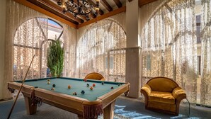 A pool table with balls, a chair, and a plant in a room with patterned curtains and wooden beams. - Diana Hotel Zakynthos (Zakynthos)