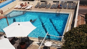 A swimming pool with lounge chairs and umbrellas, surrounded by a tiled deck. - Litsa Efi (Hersonissos)