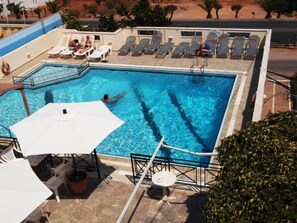 A swimming pool with lounge chairs and umbrellas, surrounded by a tiled deck. - Litsa Efi (Hersonissos)