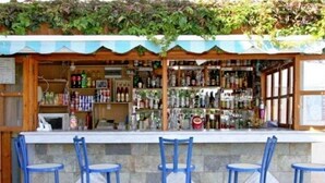 A bar area with a stone counter, blue bar stools, and shelves stocked with various bottles. - Litsa Efi (Hersonissos)