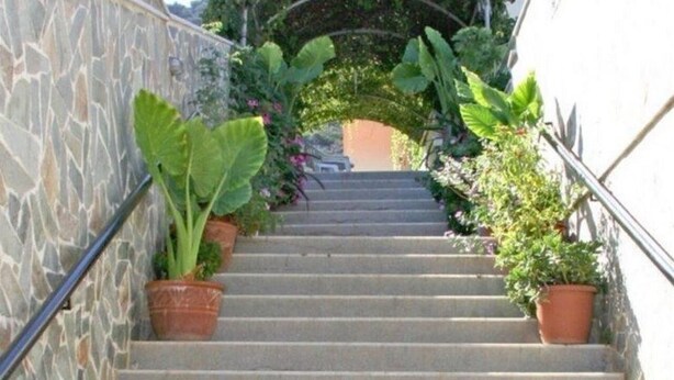 A staircase with stone walls, potted plants, and a metal handrail. - Litsa Efi (Hersonissos)