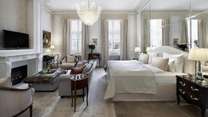 A spacious hotel room with a large bed, a sofa, a fireplace, and a television. - Hotel Sacher Wien (Vienna)