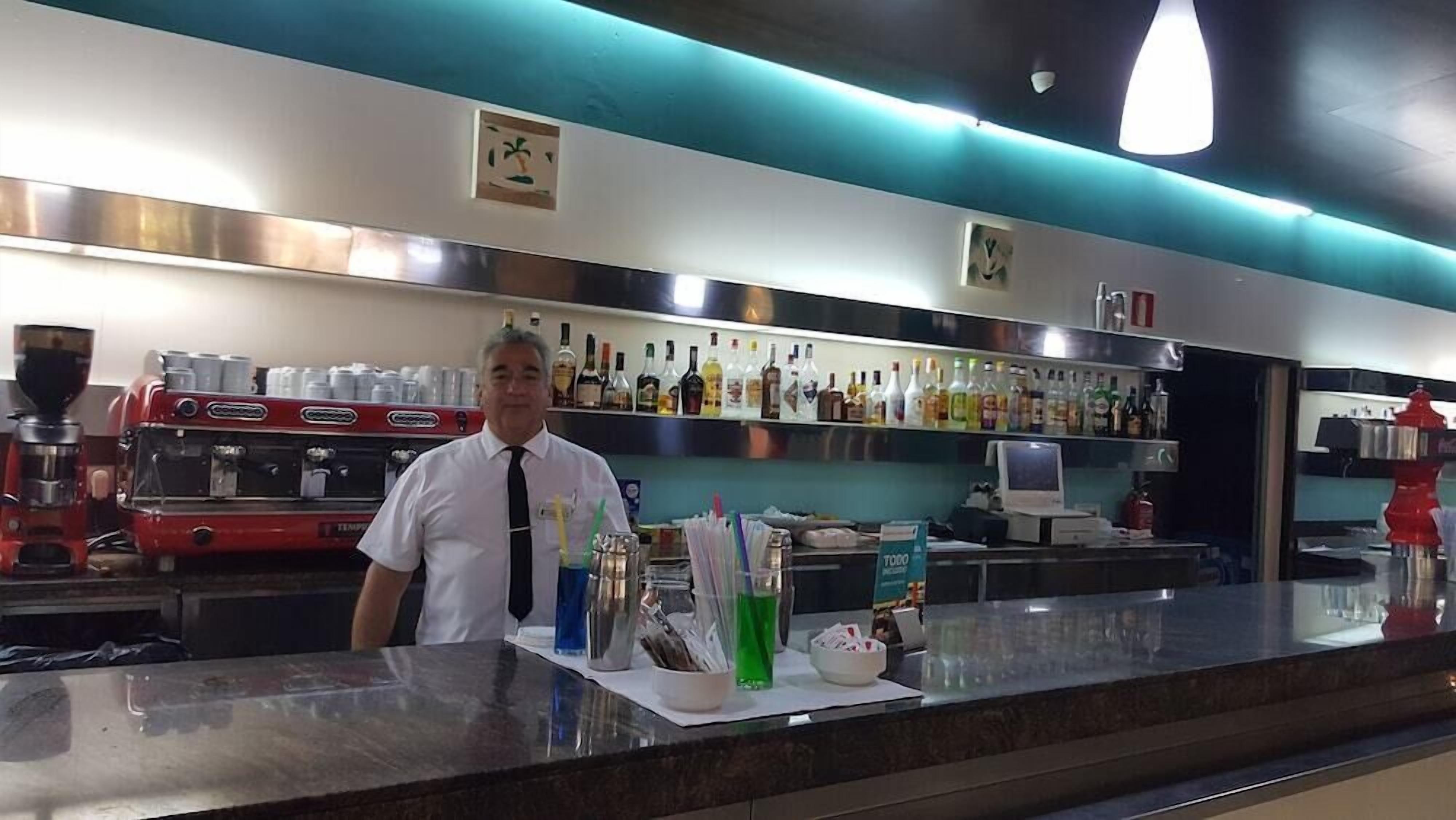 A bar area with a coffee machine, a counter with various bottles, and a computer monitor.