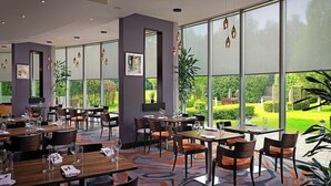 A restaurant with large windows, modern furniture, and a view of a garden. - Carlton Hotel Blanchardstown (Dublin)