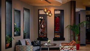 A modern lobby with a sofa, patterned ottoman, and a round table with a vase of flowers. - Carlton Hotel Blanchardstown (Dublin)