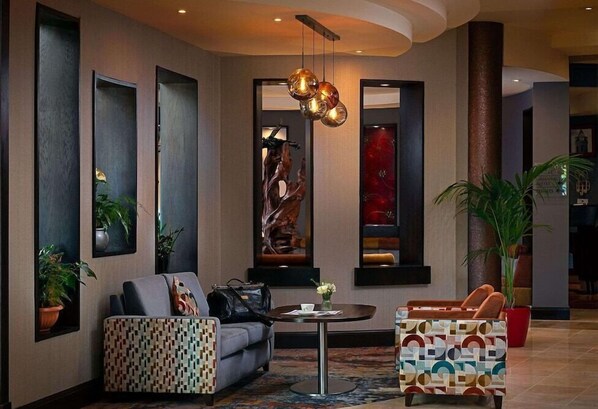 A modern lobby with a sofa, patterned ottoman, and a round table with a vase of flowers.